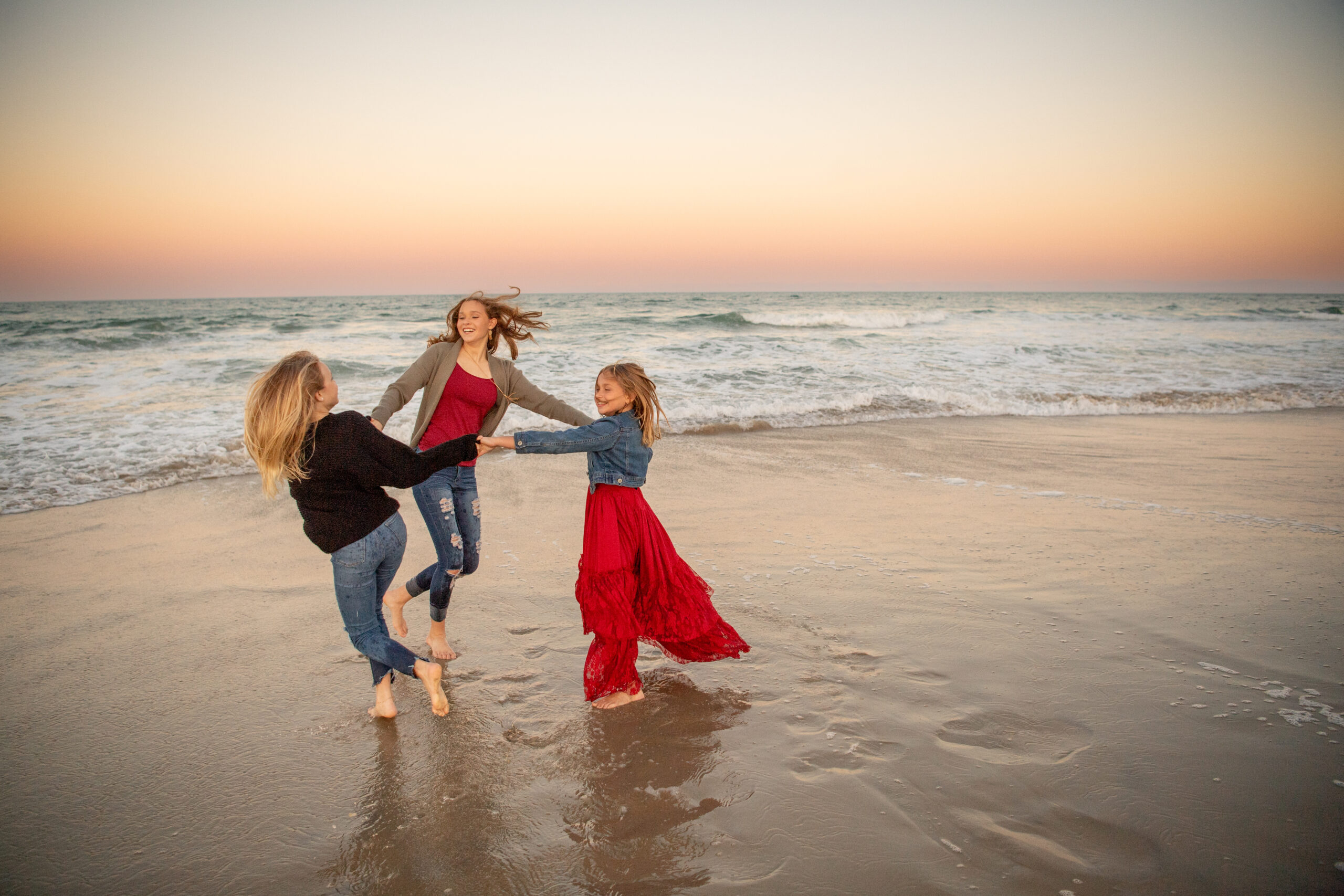 Three little girls dancing on the beach at the OBX for their beach family session.